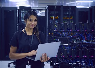 Portrait of smiling female technician using laptop in server room