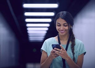 Smiling female technician looking at smart phone in data center