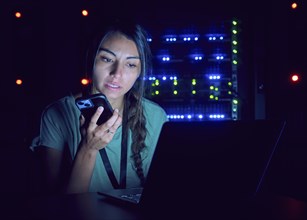 Female technician using laptop and smart phone in server room