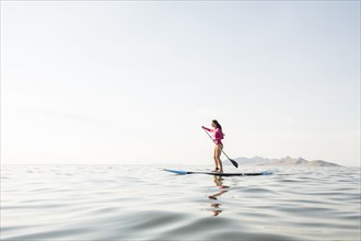 Woman in pink swimsuit paddleboarding on lake