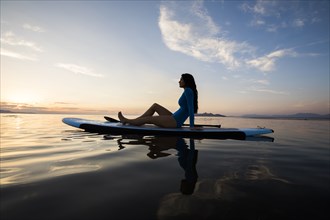 Woman in sitting on paddleboard on lake at sunset