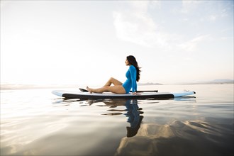Portrait of woman in blue swimsuit sitting on paddleboard on lake at sunset
