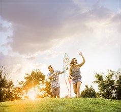 Smiling couple flying kite in park at sunset