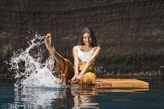 Beautiful woman splashing water on wooden raft in cenote