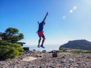 Man jumping on cliff with arms raised