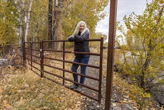 Senior blonde woman leaning on ranch gate