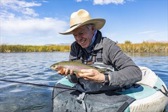 Senior fly fisherman holds rainbow trout before releasing back into spring creek