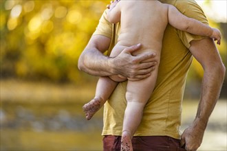 Father holding naked son outdoors