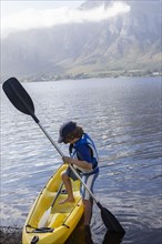 Boy entering kayak in lagoon