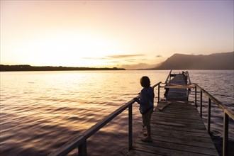 Boy standing on pier at lagoon at sunset