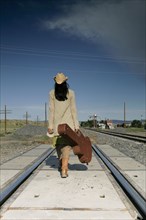 Woman with guitar walking down railroad tracks