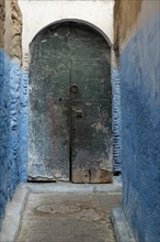 Colorful blue walls and old door in alleyway in medina