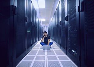 Female technician using laptop and phone in server room