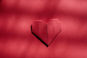 Red origami heart on red background