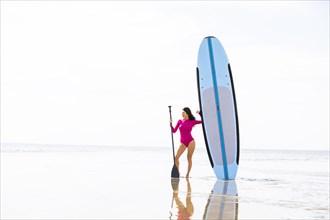 Woman standing next to paddleboard on sandy beach