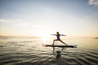 Woman doing yoga on paddleboard at sunset
