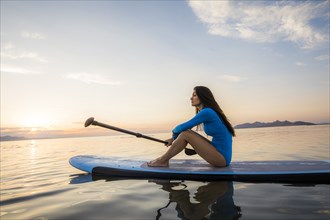 Woman sitting on paddleboard at sunset