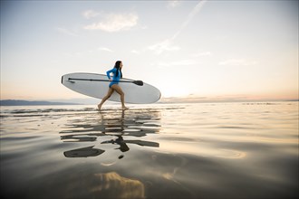 Woman running on beach with paddleboard at sunset