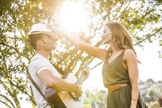 Woman putting fedora hat on man playing acoustic guitar in park