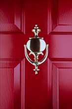 Close-up of old fashioned brass door knocker on red front door