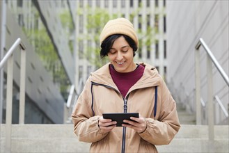 Smiling woman holding digital tablet on steps in city