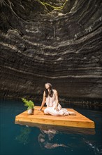 Woman sitting on floating dock near rocky coast