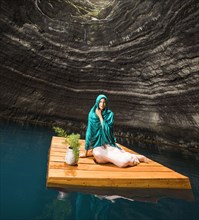 Portrait of woman sitting on floating dock near rocky coast