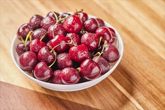 Fresh cherries in bowl on wooden surface