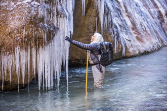 Senior woman exploring icicles while hiking in mountains