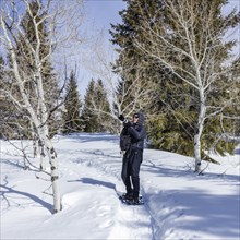 Senior woman wearing snowshoes hiking in snowy forest