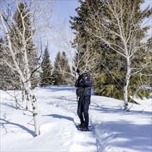 Senior woman wearing snowshoes hiking in snowy forest