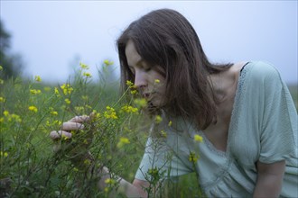 Woman smelling flowers in meadow on foggy day