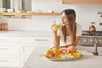 Woman drinking fresh citrus juice in kitchen