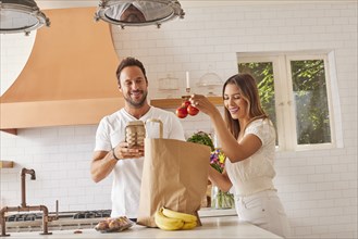 Smiling couple with paper shopping bag and groceries in kitchen