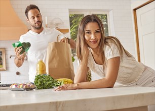 Smiling couple with paper shopping bag and groceries in kitchen