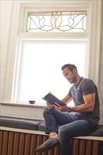 Man reading book and by window at home