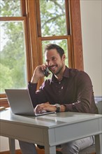 Smiling man using laptop and smart phone at table at home