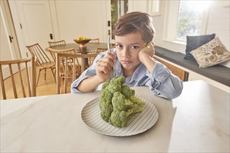 Displeased boy looking at broccoli on plate