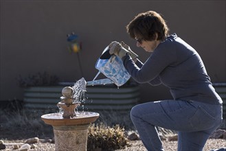 Woman filling bird bath with watering can