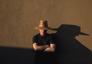 Senior man in straw hat casting shadow on wall