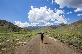 Senior woman standing with arms outstretched on road in mountain scenery