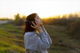 Side view of woman listening to music with closed eyes in meadow at sunset