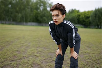 Portrait of young woman standing with hands on knees during sports training