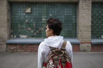Rear view of young woman looking away while standing with backpack in city