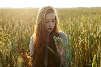 Portrait of young woman looking at cereal plants in field