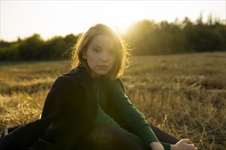 Portrait of young woman sitting in field at sunset