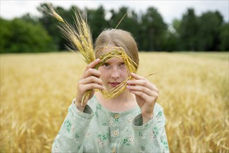 Young woman holding small wreath of wheat in field