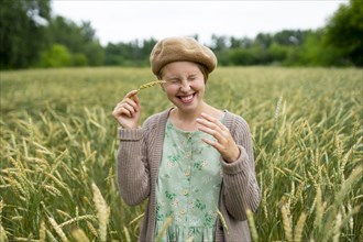 Smiling woman with closed eyes touching face with ear of wheat