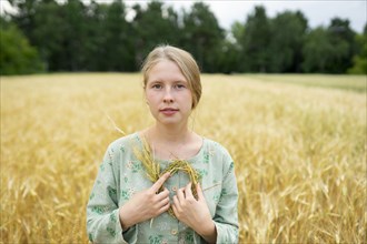 Portrait of young woman holding small wreath in wheat field