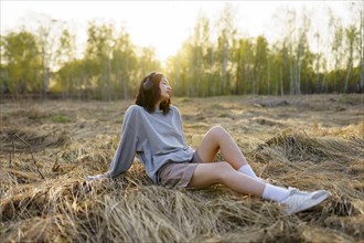 Brunette woman sitting in meadow and listening to music